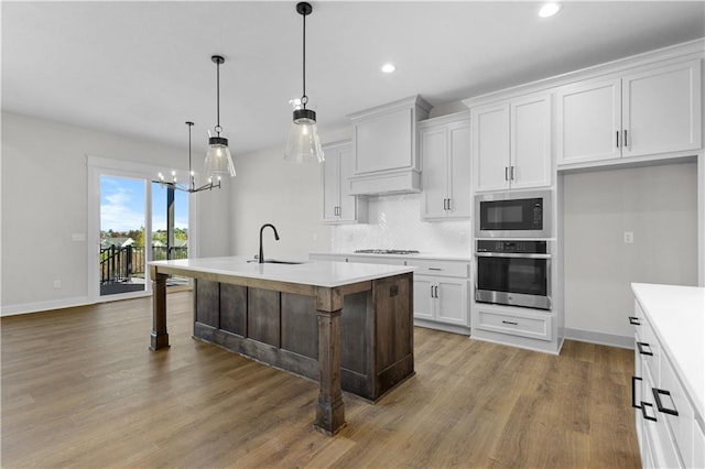 kitchen with oven, dark hardwood / wood-style flooring, a kitchen island with sink, built in microwave, and pendant lighting