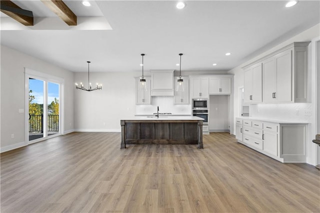 kitchen featuring appliances with stainless steel finishes, light hardwood / wood-style flooring, a kitchen island with sink, and decorative light fixtures