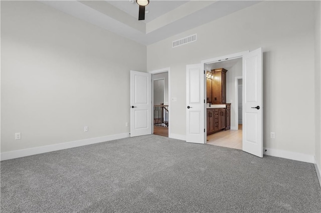 unfurnished bedroom featuring connected bathroom, ceiling fan, light carpet, and a towering ceiling