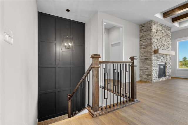 stairs with a stone fireplace, beam ceiling, and hardwood / wood-style flooring