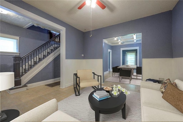 living room featuring tile patterned floors, baseboards, stairs, and a ceiling fan