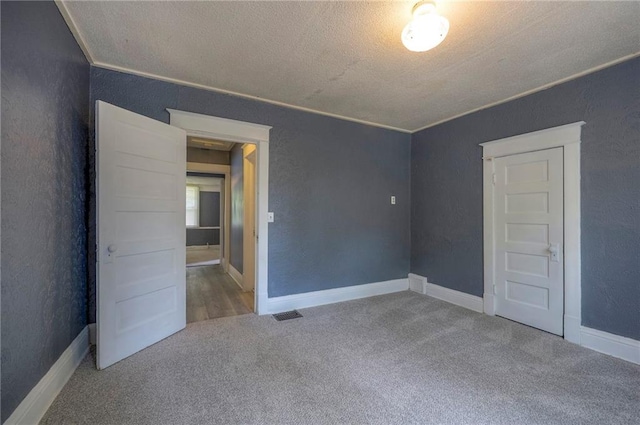 unfurnished bedroom with carpet flooring, a textured ceiling, baseboards, and a textured wall