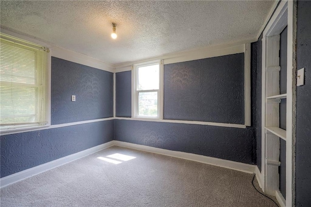 carpeted spare room featuring a textured ceiling, baseboards, and a textured wall