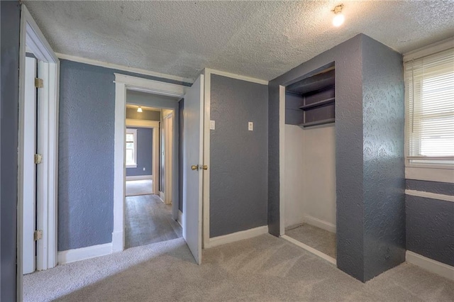 hallway featuring baseboards, a textured ceiling, carpet flooring, and a textured wall