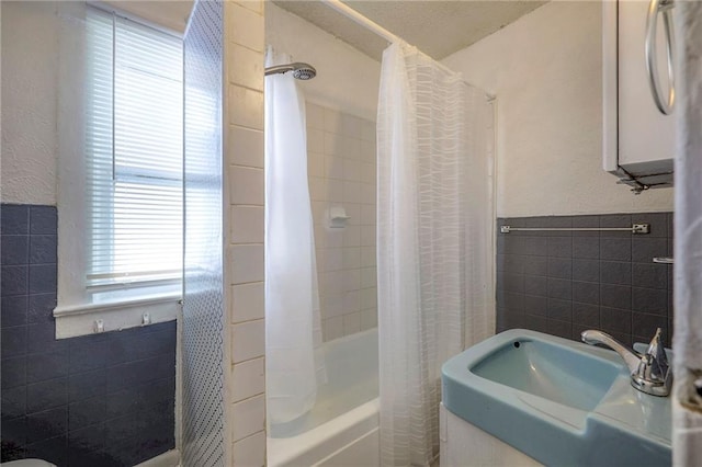 bathroom featuring a wainscoted wall, tile walls, shower / bath combo with shower curtain, and a sink