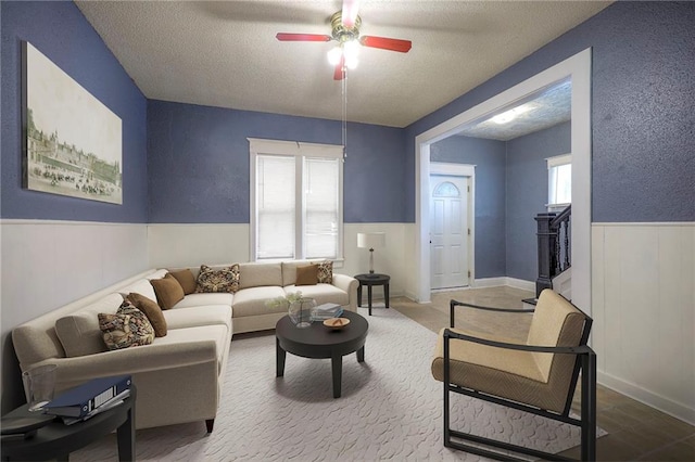 living area featuring a wainscoted wall, a textured ceiling, and ceiling fan