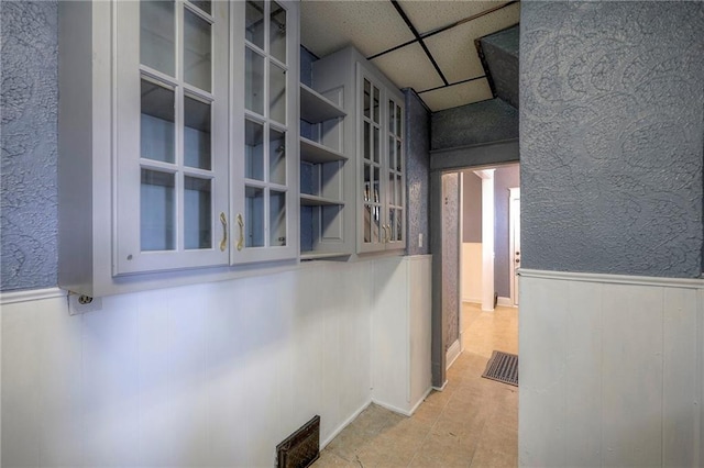 hallway with a textured wall, a wainscoted wall, visible vents, and a drop ceiling