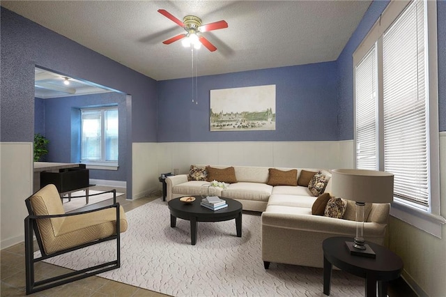 living area with a wainscoted wall, a textured ceiling, and ceiling fan