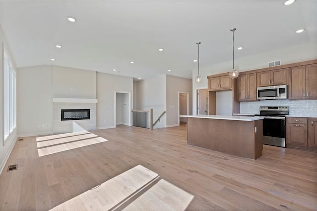 kitchen with light hardwood / wood-style flooring, appliances with stainless steel finishes, decorative light fixtures, a kitchen island, and a tiled fireplace