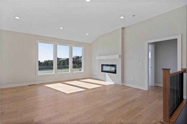 unfurnished living room with light wood-type flooring, vaulted ceiling, and a tiled fireplace