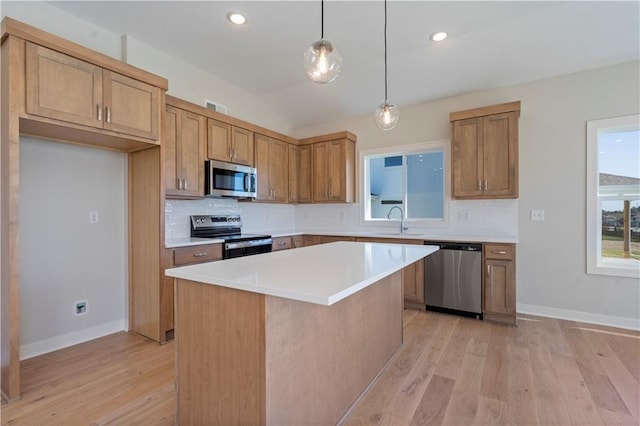 kitchen with appliances with stainless steel finishes, sink, pendant lighting, light hardwood / wood-style flooring, and a kitchen island