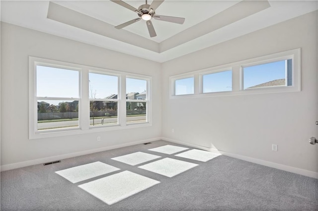 carpeted spare room featuring a tray ceiling and ceiling fan