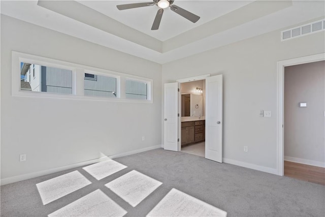 unfurnished bedroom with light carpet, ensuite bathroom, a raised ceiling, and ceiling fan