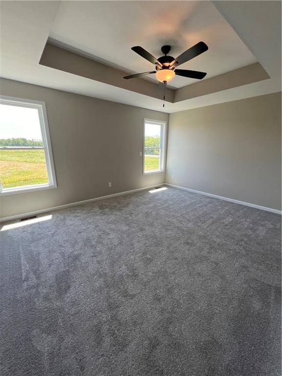 carpeted spare room with a raised ceiling and ceiling fan