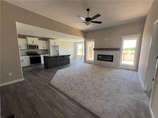 unfurnished living room with dark carpet, ceiling fan, a wealth of natural light, and a fireplace