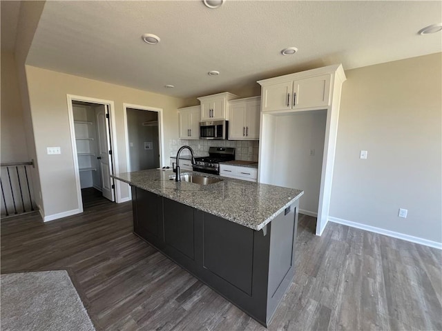 kitchen with dark hardwood / wood-style floors, range with gas cooktop, a kitchen island with sink, sink, and decorative backsplash