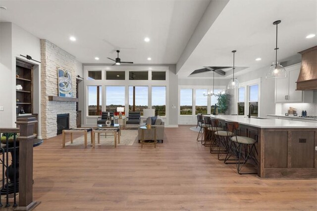 kitchen with ceiling fan, a fireplace, white cabinetry, light hardwood / wood-style flooring, and hanging light fixtures