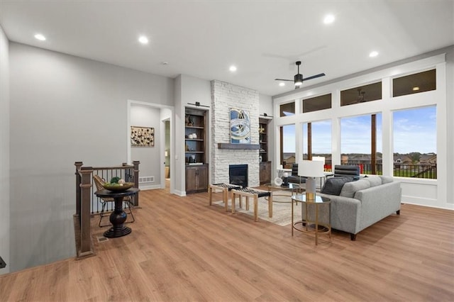 living room with ceiling fan, light hardwood / wood-style floors, and a stone fireplace