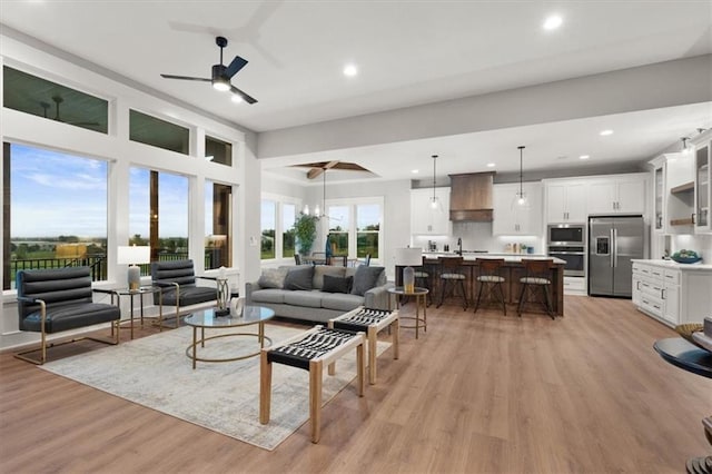 living room featuring ceiling fan with notable chandelier, sink, and light wood-type flooring