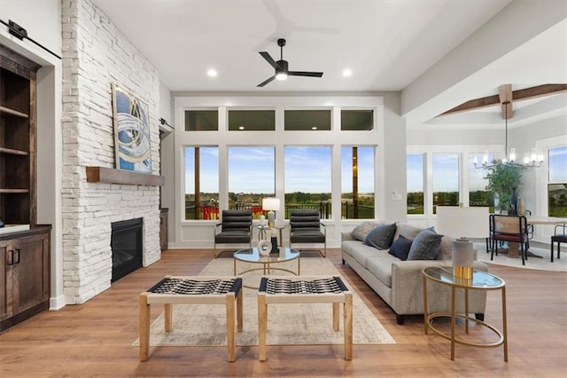 living room featuring ceiling fan with notable chandelier, light hardwood / wood-style flooring, and a stone fireplace