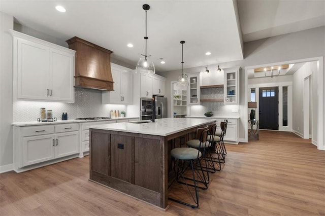 kitchen with custom exhaust hood, a breakfast bar area, an island with sink, and white cabinetry