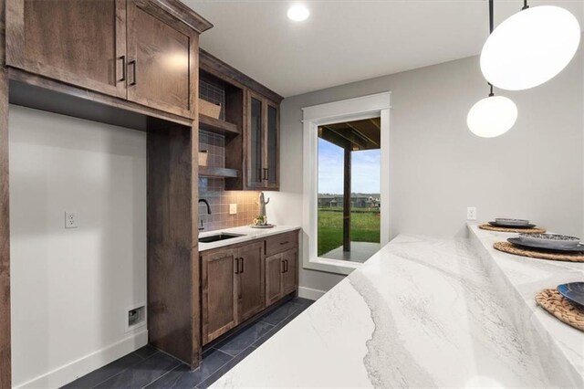 kitchen featuring decorative light fixtures, backsplash, sink, dark brown cabinetry, and light stone countertops