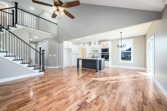 unfurnished living room featuring ceiling fan with notable chandelier, light hardwood / wood-style floors, sink, and high vaulted ceiling