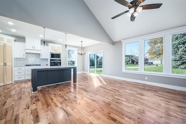 kitchen with white cabinets, an island with sink, decorative light fixtures, light hardwood / wood-style floors, and stainless steel appliances