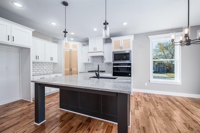 kitchen with light stone countertops, stainless steel microwave, black oven, decorative backsplash, and white cabinets