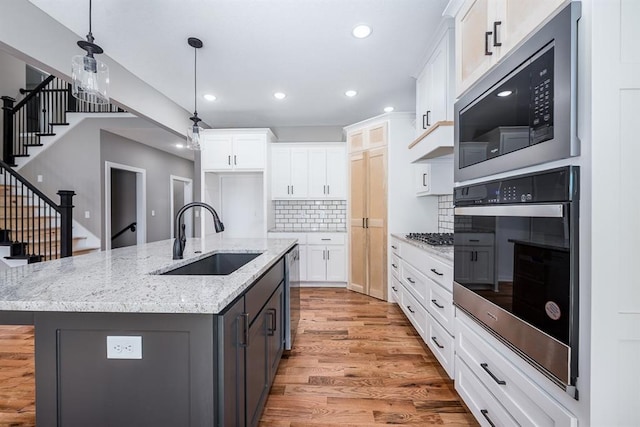 kitchen featuring white cabinets, a center island with sink, sink, light hardwood / wood-style flooring, and stainless steel appliances