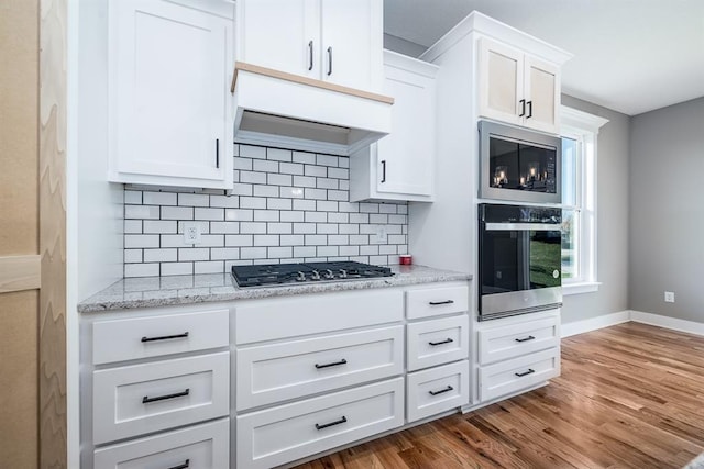 kitchen with decorative backsplash, hardwood / wood-style floors, white cabinets, and stainless steel appliances