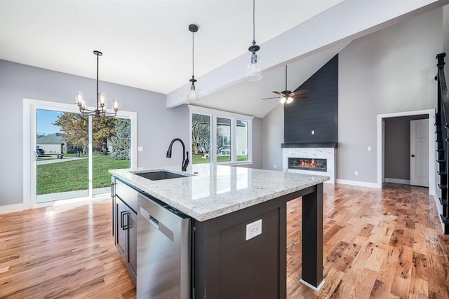 kitchen with a kitchen island with sink, stainless steel dishwasher, light stone countertops, a fireplace, and light hardwood / wood-style floors