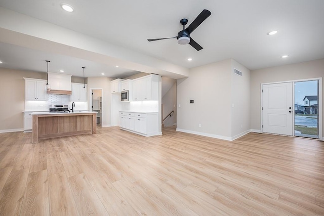 unfurnished living room with light wood-type flooring, ceiling fan, and sink