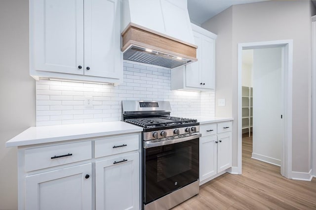 kitchen with custom exhaust hood, stainless steel gas range oven, white cabinets, light hardwood / wood-style flooring, and decorative backsplash