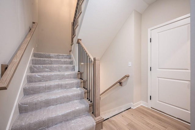 stairway with wood-type flooring and vaulted ceiling