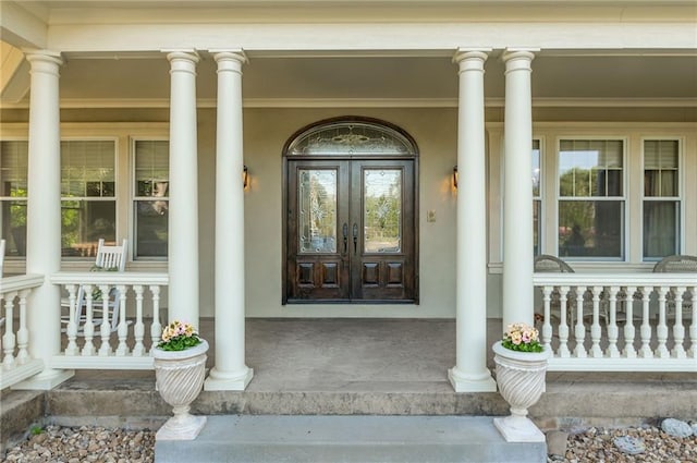 doorway to property with covered porch, french doors, and stucco siding