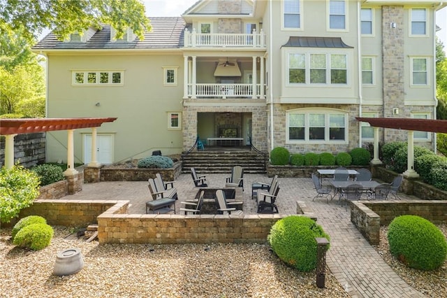 rear view of house with stone siding, an outdoor fire pit, a patio, and a balcony