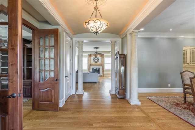 foyer featuring lofted ceiling, wood finished floors, baseboards, a glass covered fireplace, and decorative columns