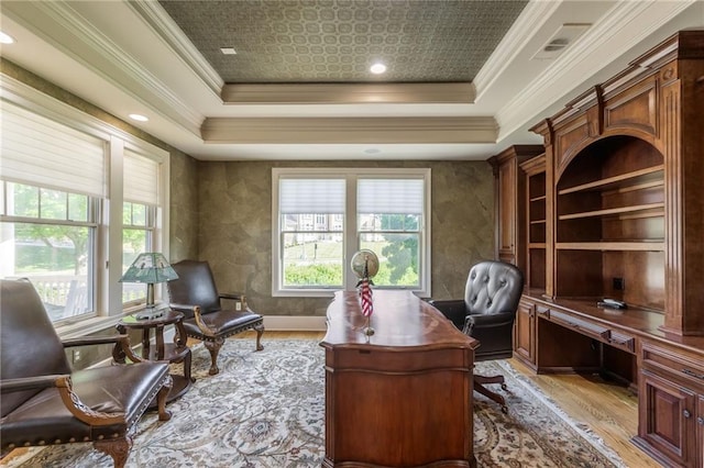 office area with light wood-style floors, a tray ceiling, and a healthy amount of sunlight