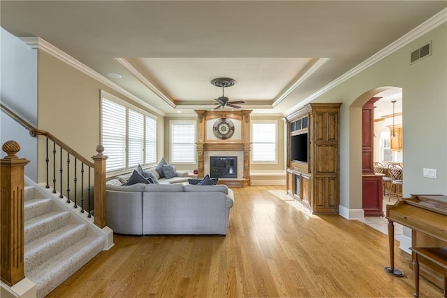 living room featuring light wood finished floors, a raised ceiling, visible vents, stairway, and a glass covered fireplace