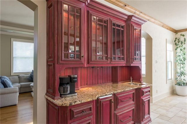 kitchen featuring arched walkways, light stone countertops, crown molding, dark brown cabinets, and a sink