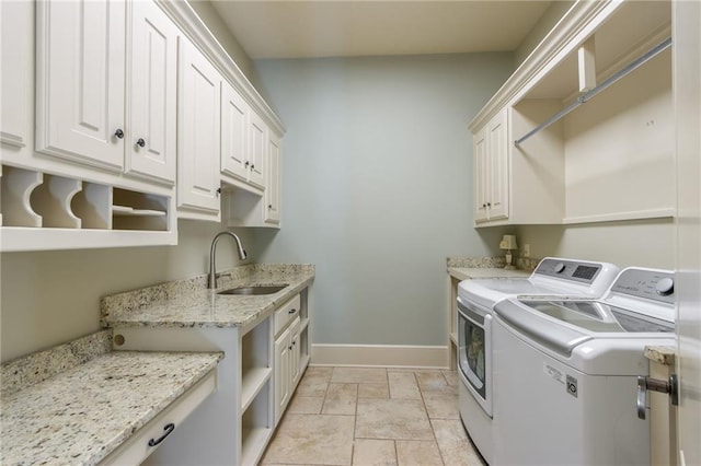 laundry room featuring washing machine and dryer, a sink, baseboards, cabinet space, and stone finish floor