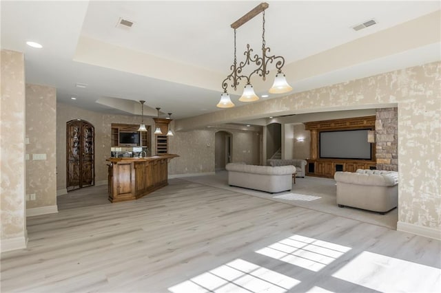 unfurnished living room featuring arched walkways, visible vents, stairs, a tray ceiling, and wallpapered walls