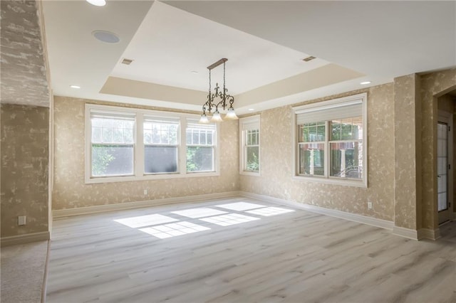 empty room with baseboards, a tray ceiling, wood finished floors, and wallpapered walls