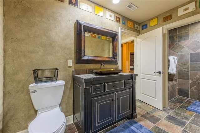 full bathroom featuring visible vents, toilet, vanity, and stone tile floors