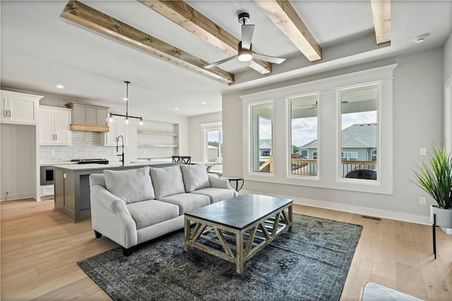 living room featuring ceiling fan, sink, light wood-type flooring, and beam ceiling