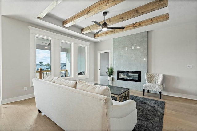 living room with light hardwood / wood-style floors, a fireplace, beam ceiling, and ceiling fan