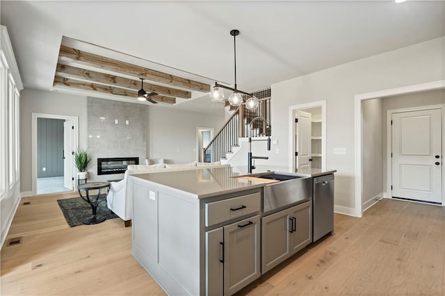 kitchen with light hardwood / wood-style floors, an island with sink, a fireplace, pendant lighting, and stainless steel dishwasher