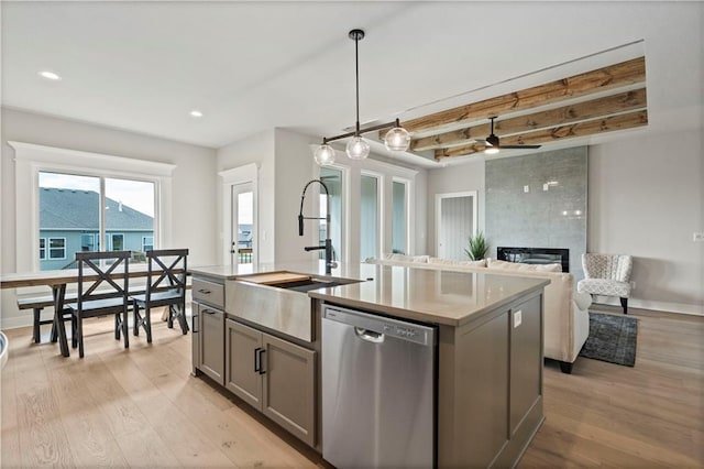 kitchen featuring pendant lighting, beam ceiling, stainless steel dishwasher, a kitchen island with sink, and a large fireplace