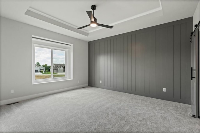 carpeted spare room featuring a barn door, a raised ceiling, and ceiling fan